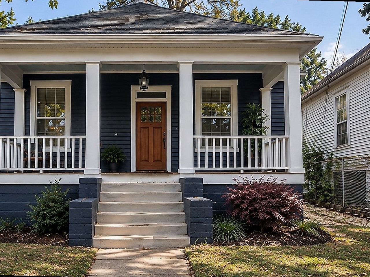 The same bungalow after renovation — new roof, navy siding, white porch columns and rail, wood front door, landscaped yard