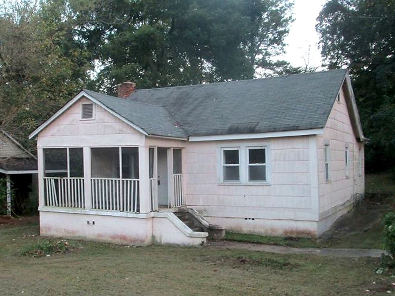 Craftsman bungalow before renovation — bare siding, overgrown lot